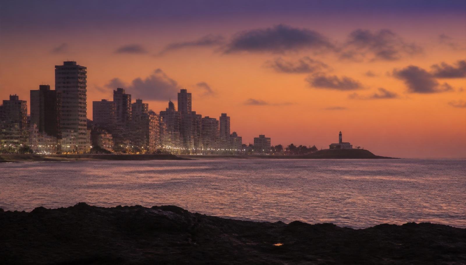 Vista panorâmica do bairro da Barra em Salvador ao entardecer, com prédios residenciais alinhados ao longo da orla e o Farol da Barra ao fundo, representando o mercado imobiliário baiano