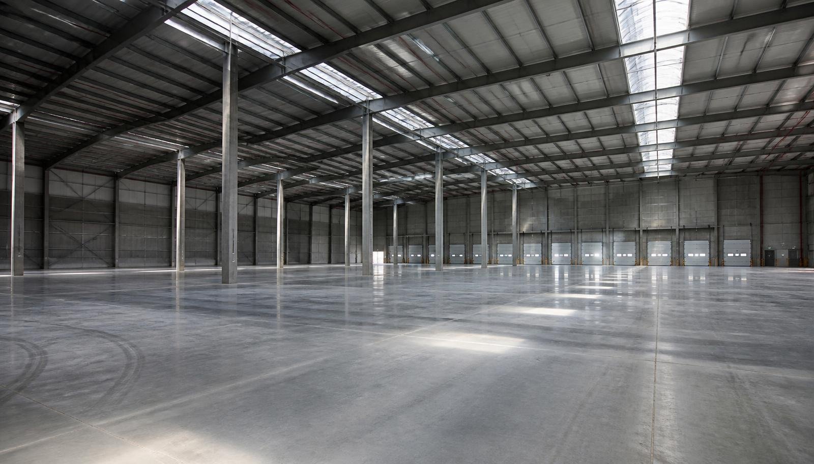 Interior de galpão logístico moderno vazio com pé-direito alto, piso de concreto polido, estrutura metálica e docas de carregamento ao fundo