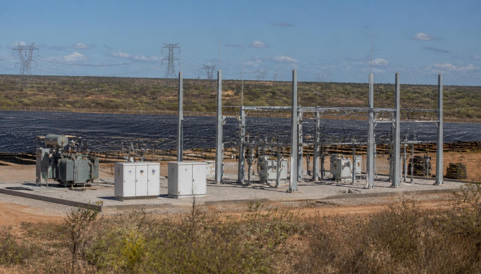 Subestação transformadora e cabines de conexão de um parque de minigeração distribuída solar na região semiárida da Bahia, com linhas de transmissão ao fundo e módulos fotovoltaicos ao redor